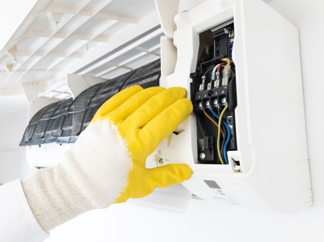 A person wearing yellow gloves is working on an air conditioner.