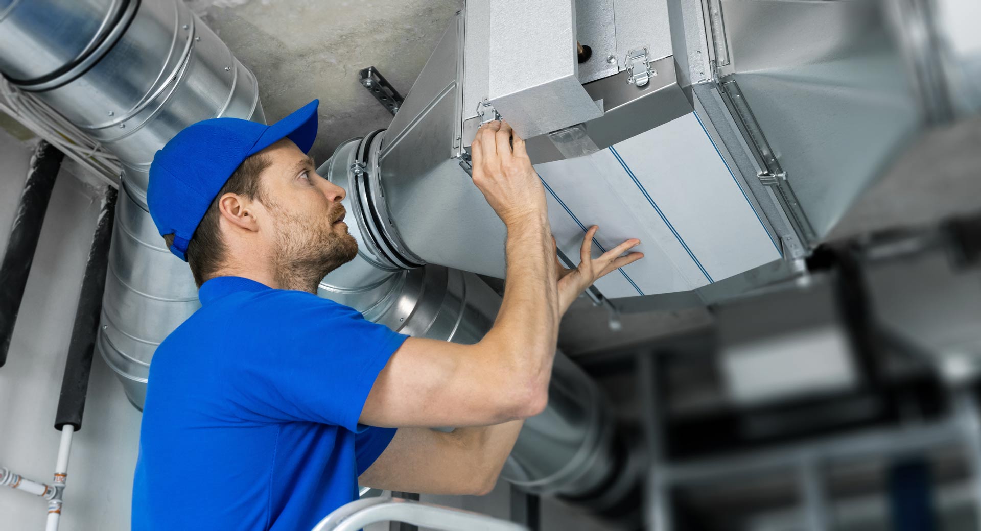 A man is working on a ventilation system in a building.