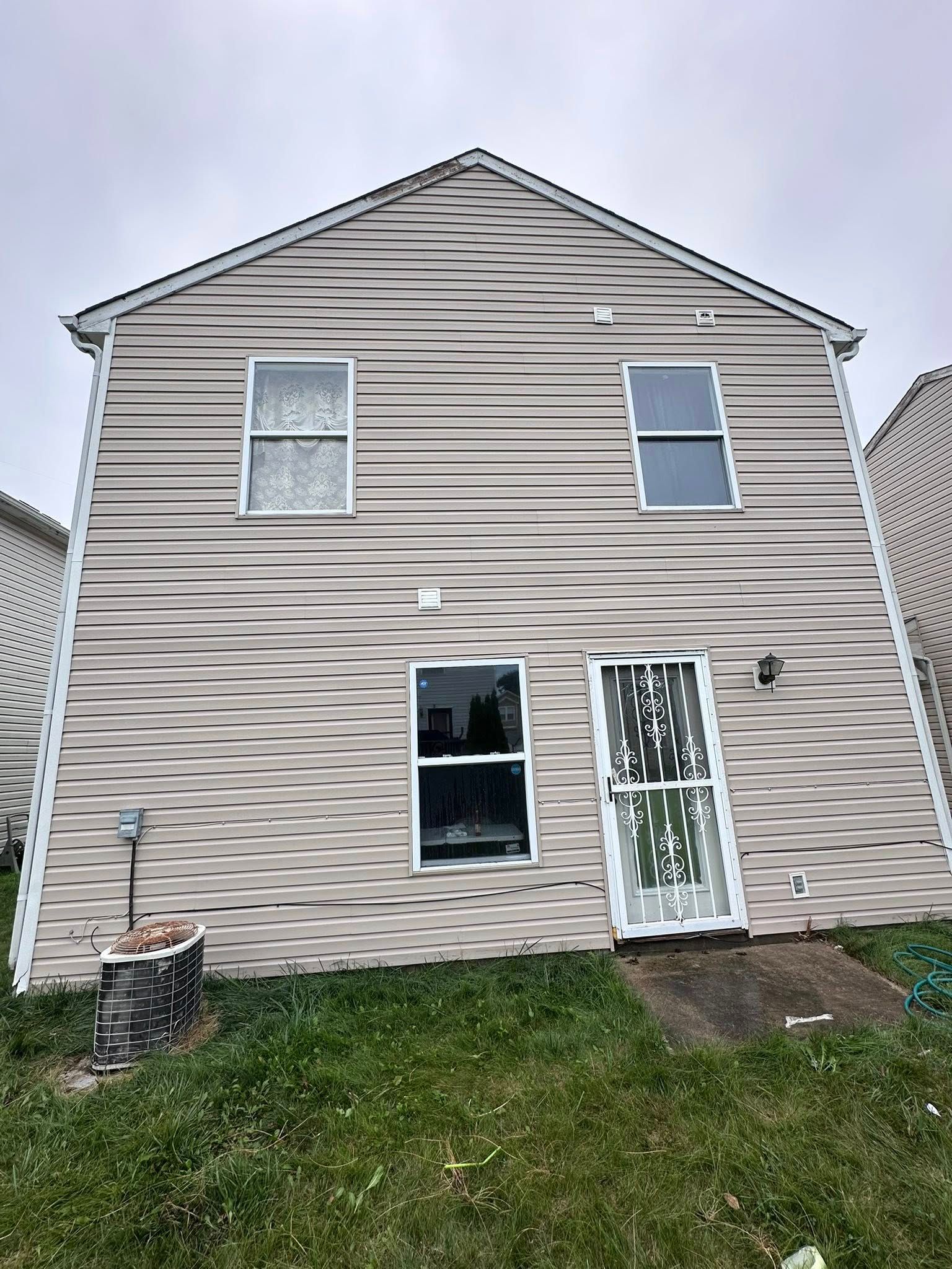 Back of a tan two-story house with white trim, windows, and a grassy yard.