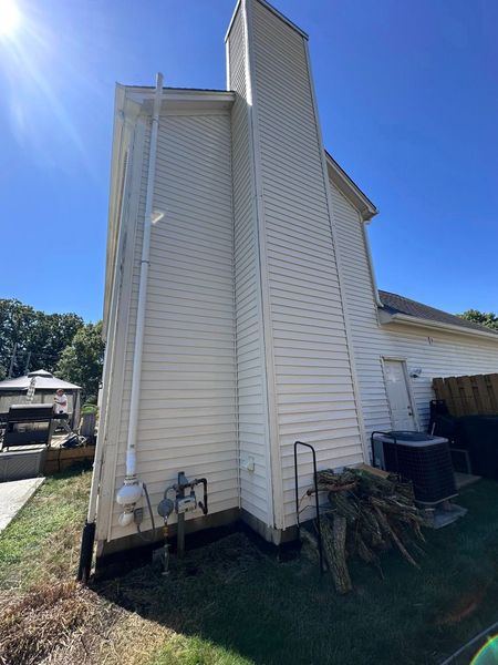 White house exterior with a tall chimney, slanted siding, and a bright blue sky.