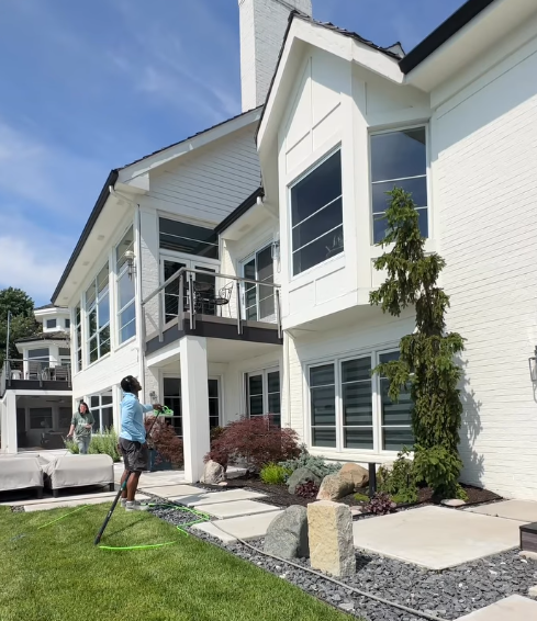 White two-story house with large windows and a person using a hose on the lawn.