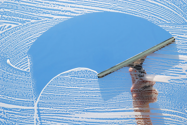Blue squeegee cleaning a frosted glass surface against a blue sky background