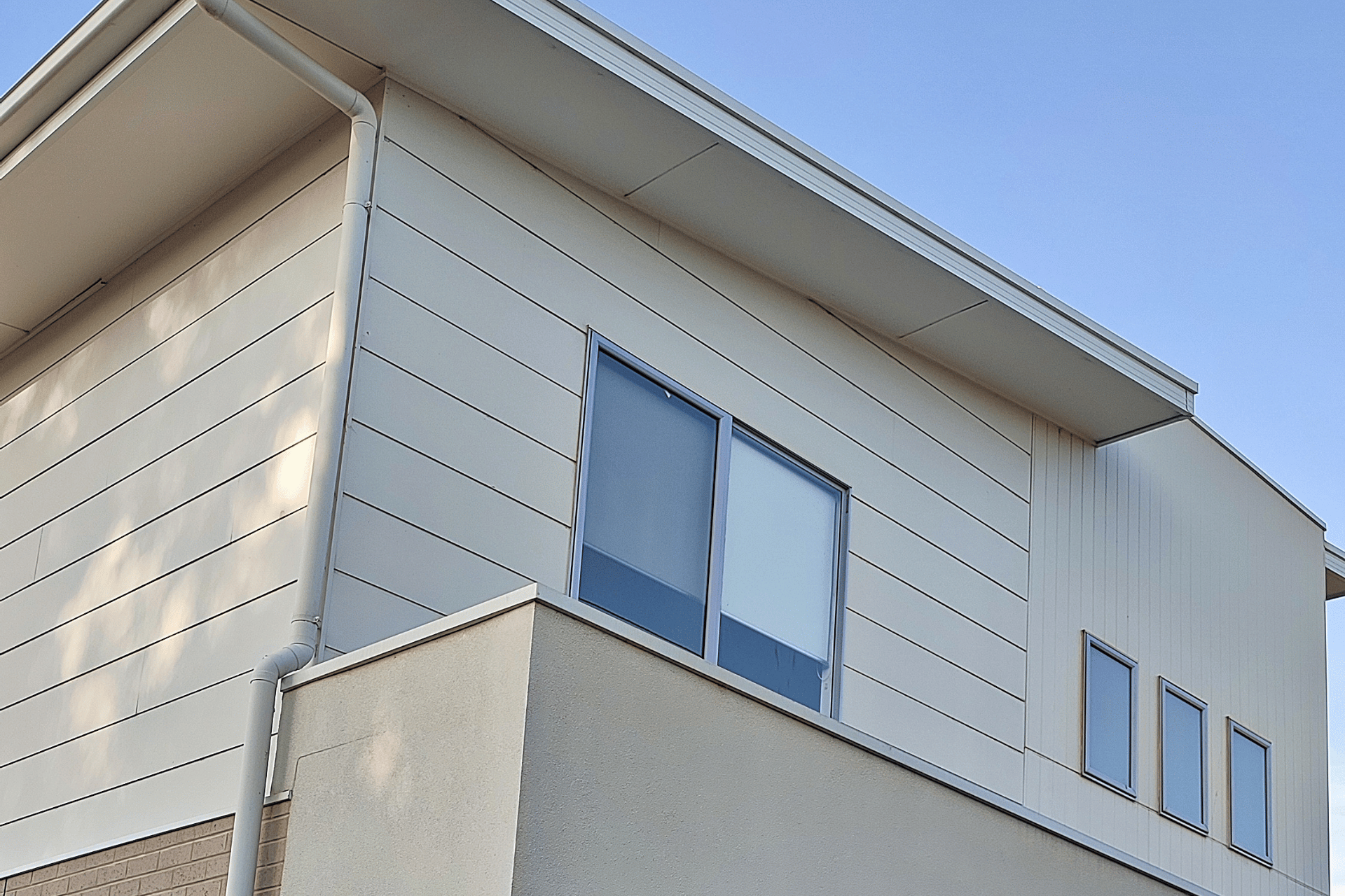 Corner view of a white apartment building with blue windows and a beige lower wall against a clear sky