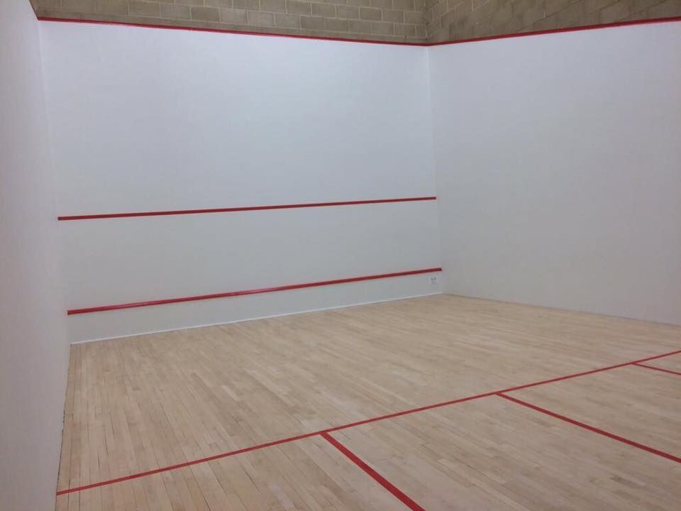 A squash court with a wooden floor and white walls.