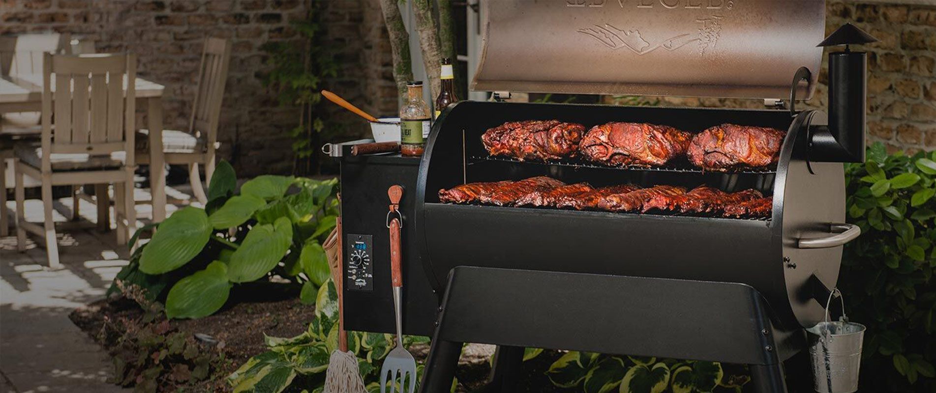 A grill is cooking meat on a patio in a backyard.