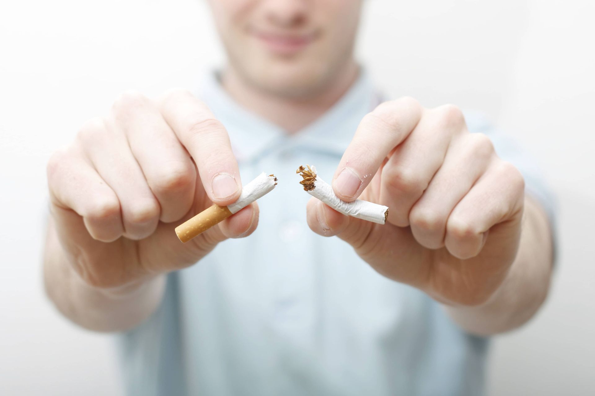 A person in a light blue shirt holds a broken cigarette between their hands, symbolizing the act of quitting smoking.