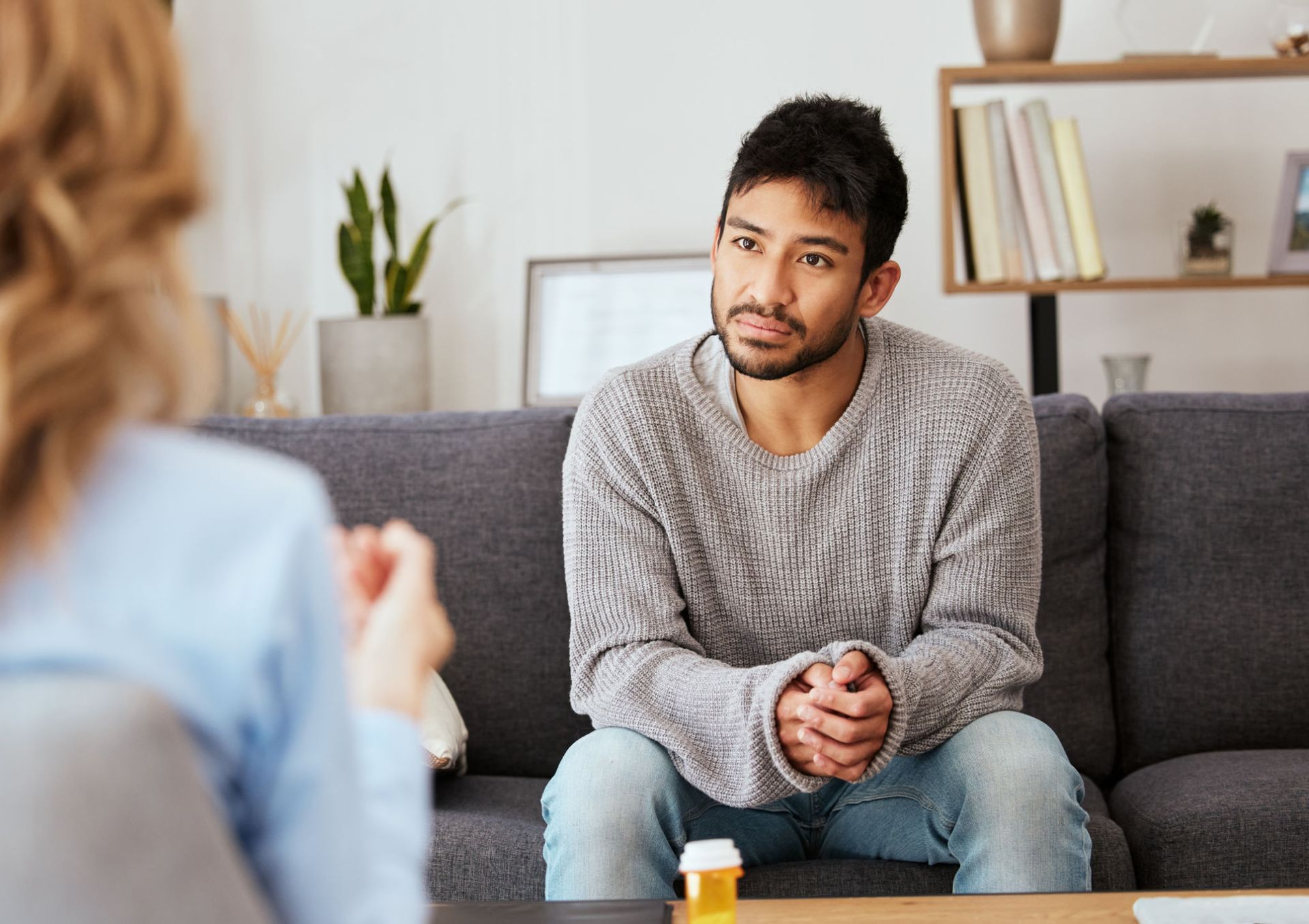 A focused person sits on a couch in a bright office, listening attentively to someone sitting across from them.