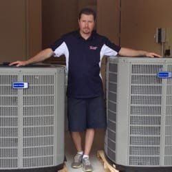 A man is standing next to two air conditioners in a garage.