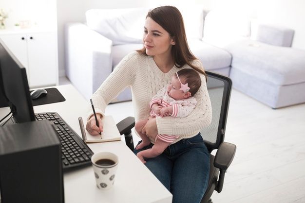 A woman is holding a baby while sitting at a desk in front of a computer.