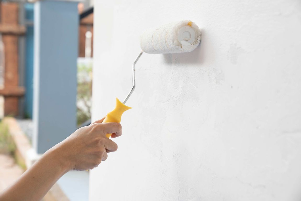 A person is painting a wall with a paint roller.