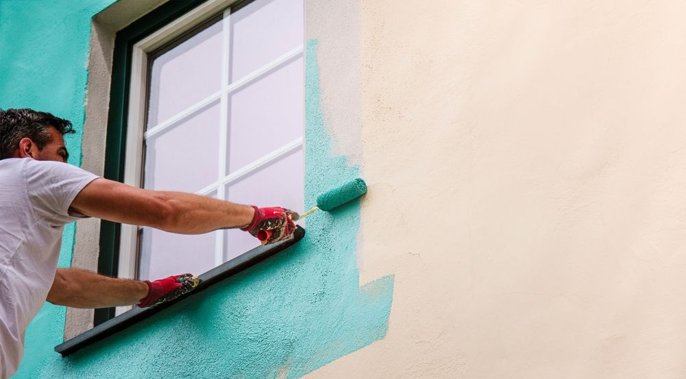 A man is painting the side of a building with a roller.