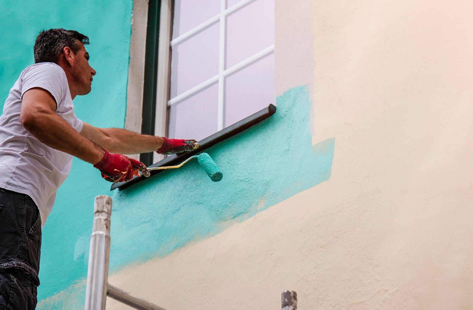 A man is painting the side of a building with a roller.