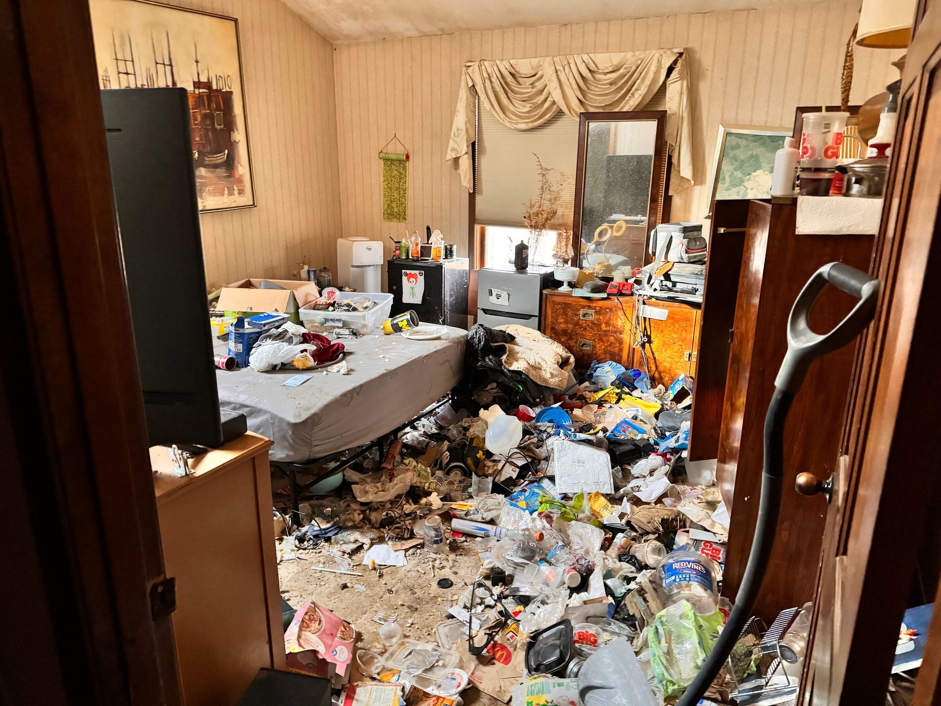 There is a vacuum cleaner in the middle of a messy room.