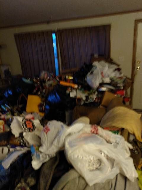 A living room filled with lots of trash bags and clothes.