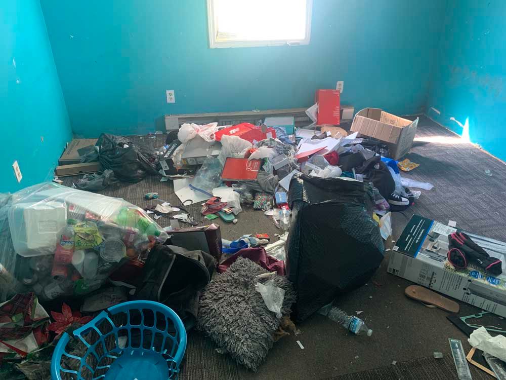 A room with a lot of trash on the floor and a blue wall.