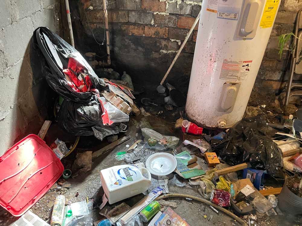 A dirty room with a water heater and trash on the floor.