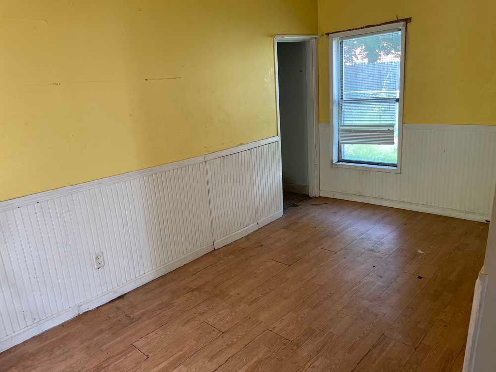 An empty room with hardwood floors , yellow walls and a window.