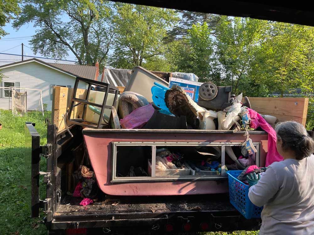 A woman is standing in front of a dumpster filled with junk.