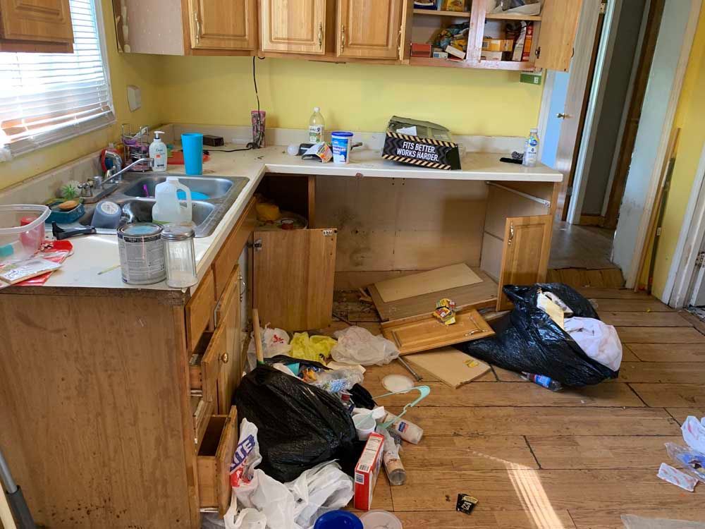 A kitchen with a lot of trash on the floor and a sink.