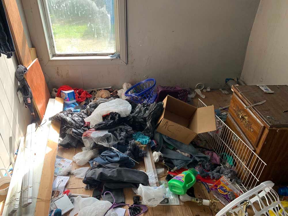 A room with a lot of trash on the floor and a window.