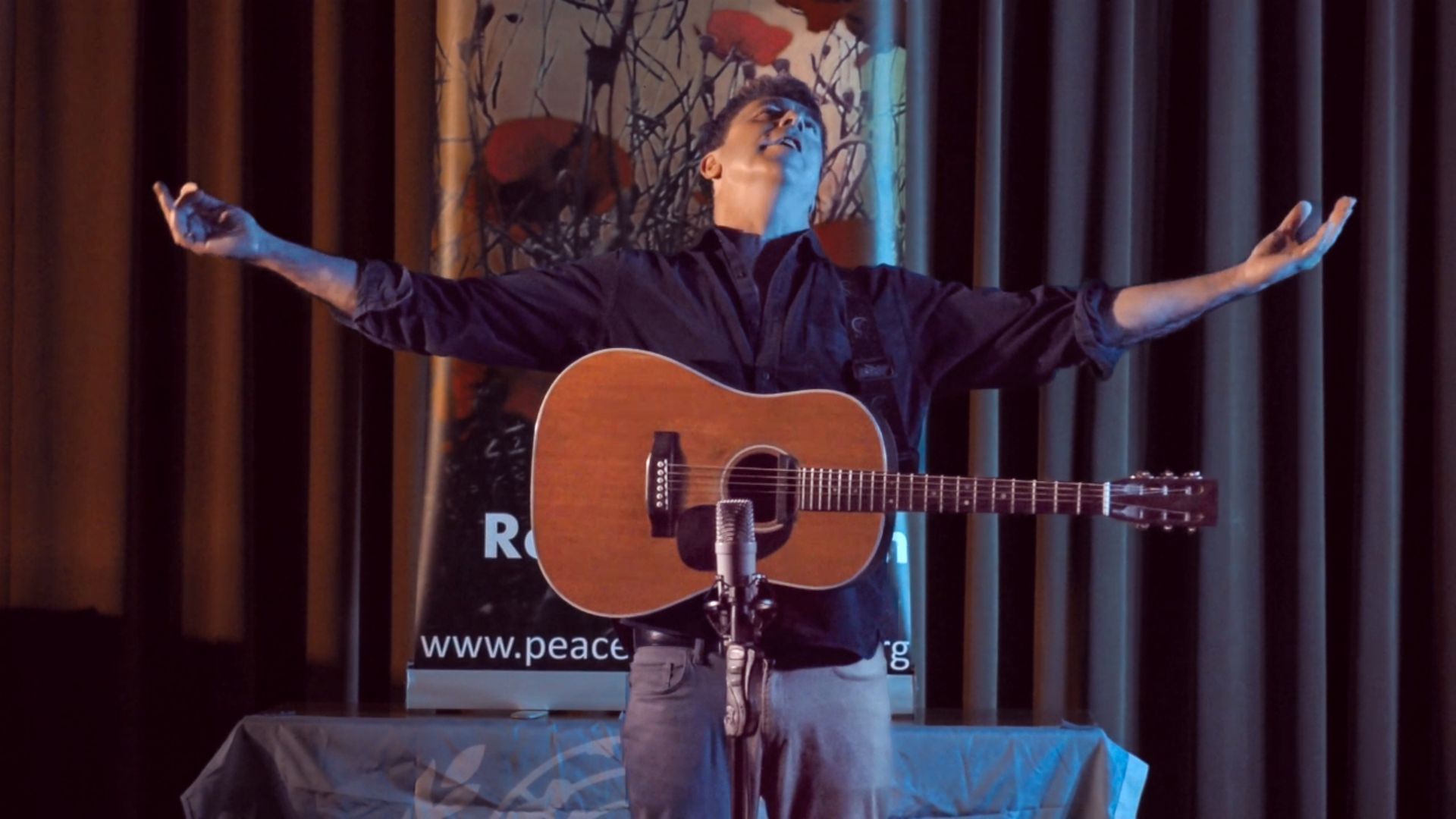 A man is playing a guitar and singing into a microphone on a stage.