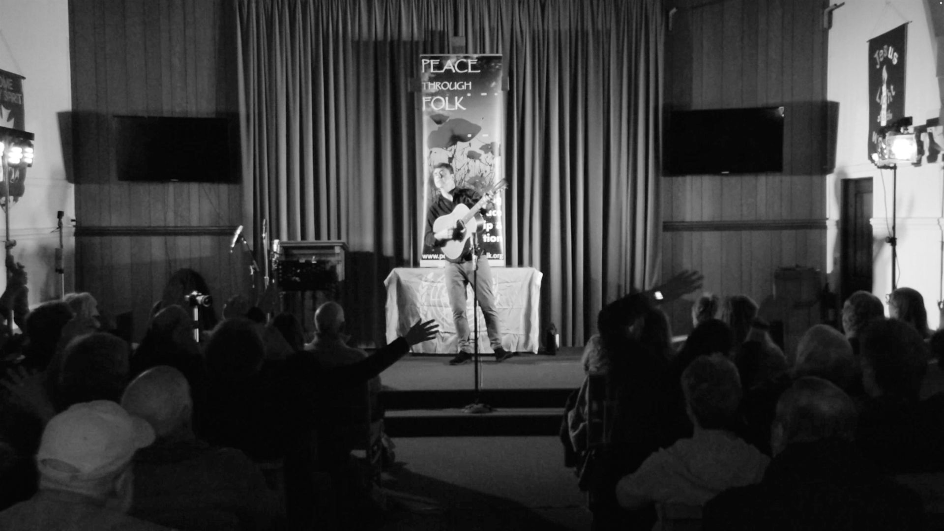A black and white photo of a man standing on a stage in front of a crowd.