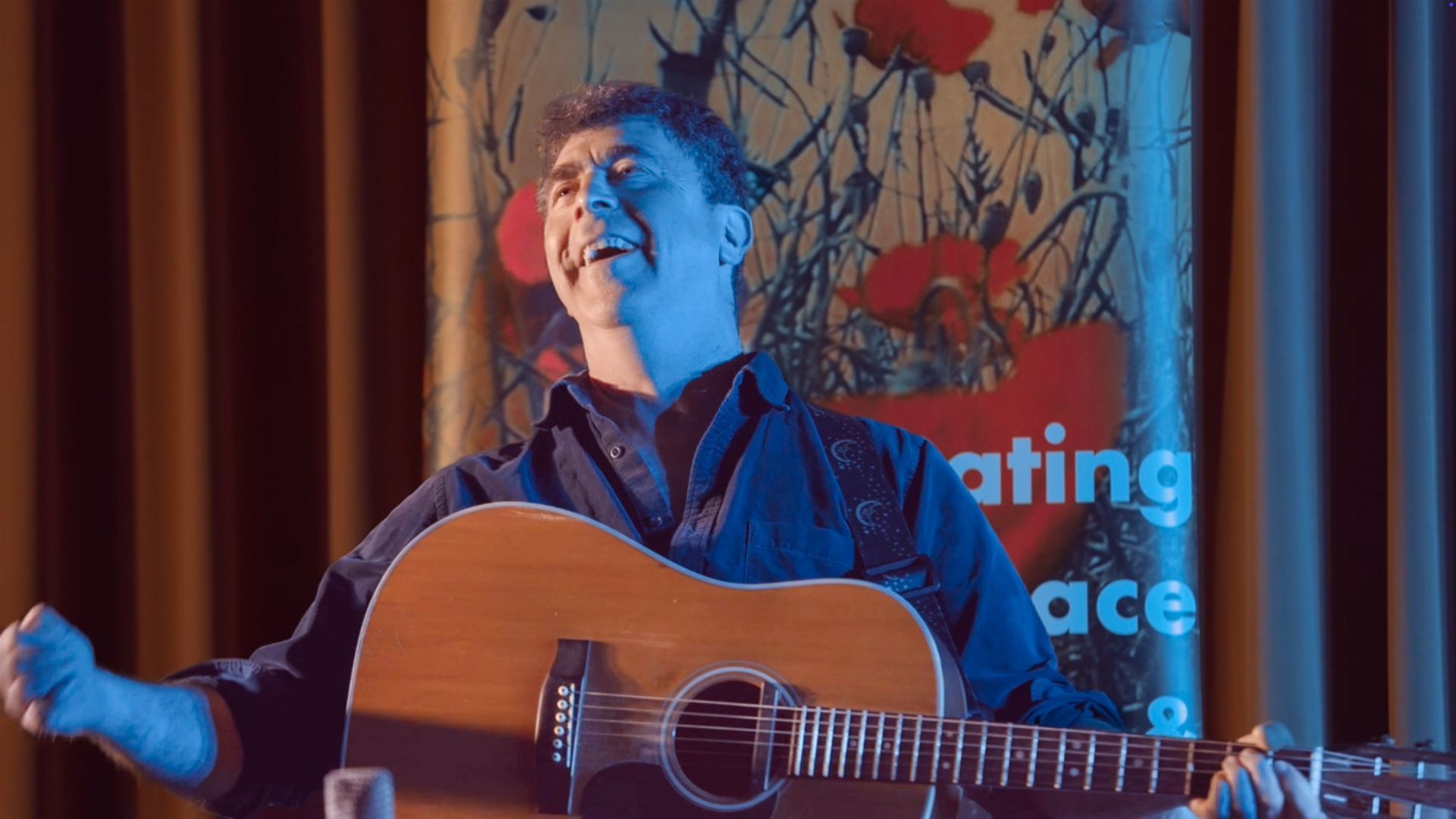 A man is holding a guitar in front of a sign that says celebrating