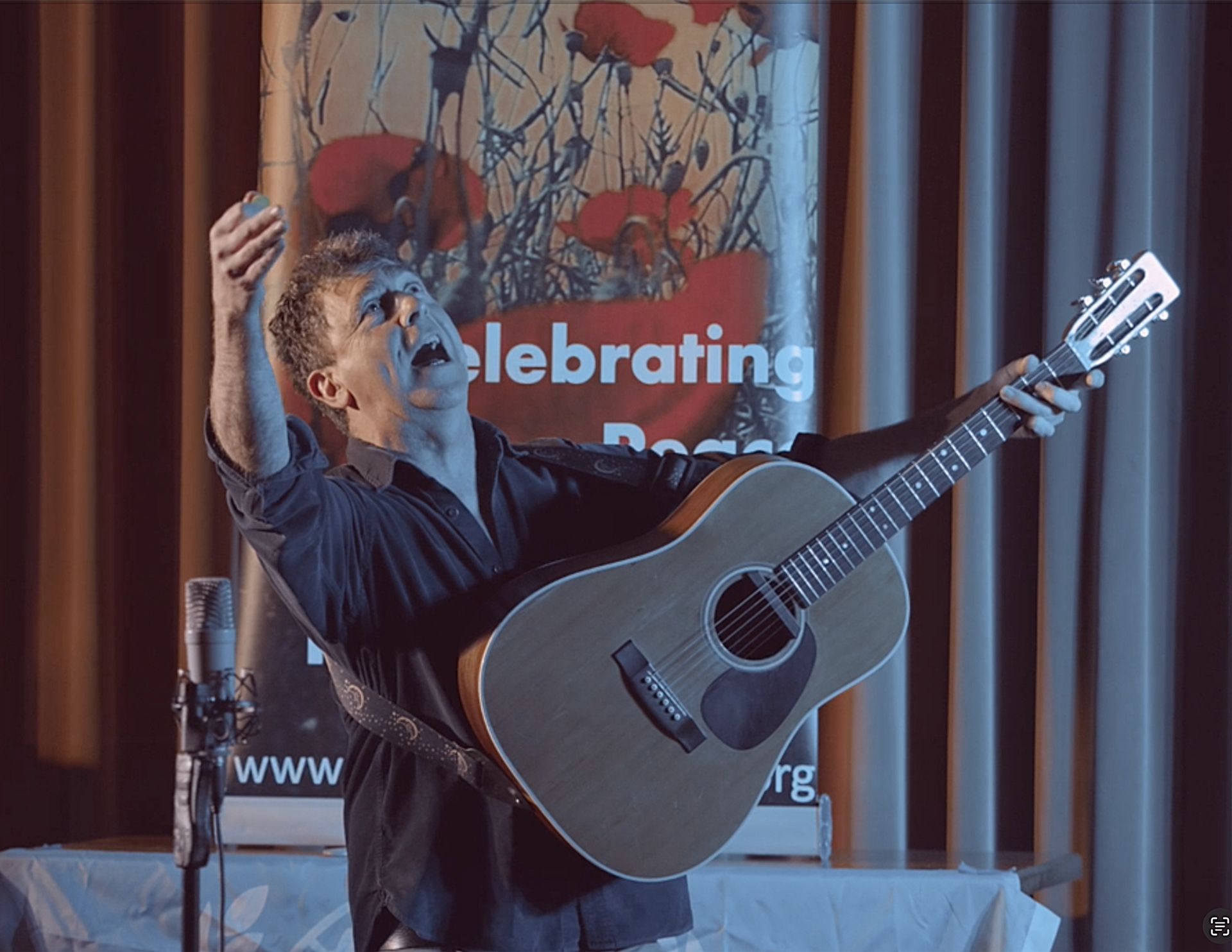 A man is holding a guitar in front of a sign that says celebrating