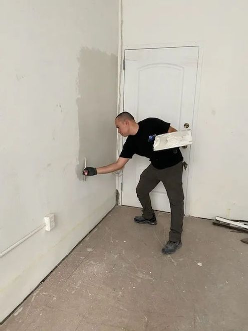 A man is plastering a wall in an empty room.