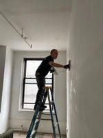 A man is standing on a ladder working on a wall.