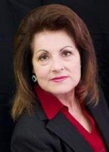 A woman is sitting at a desk with a laptop and a vase of flowers.