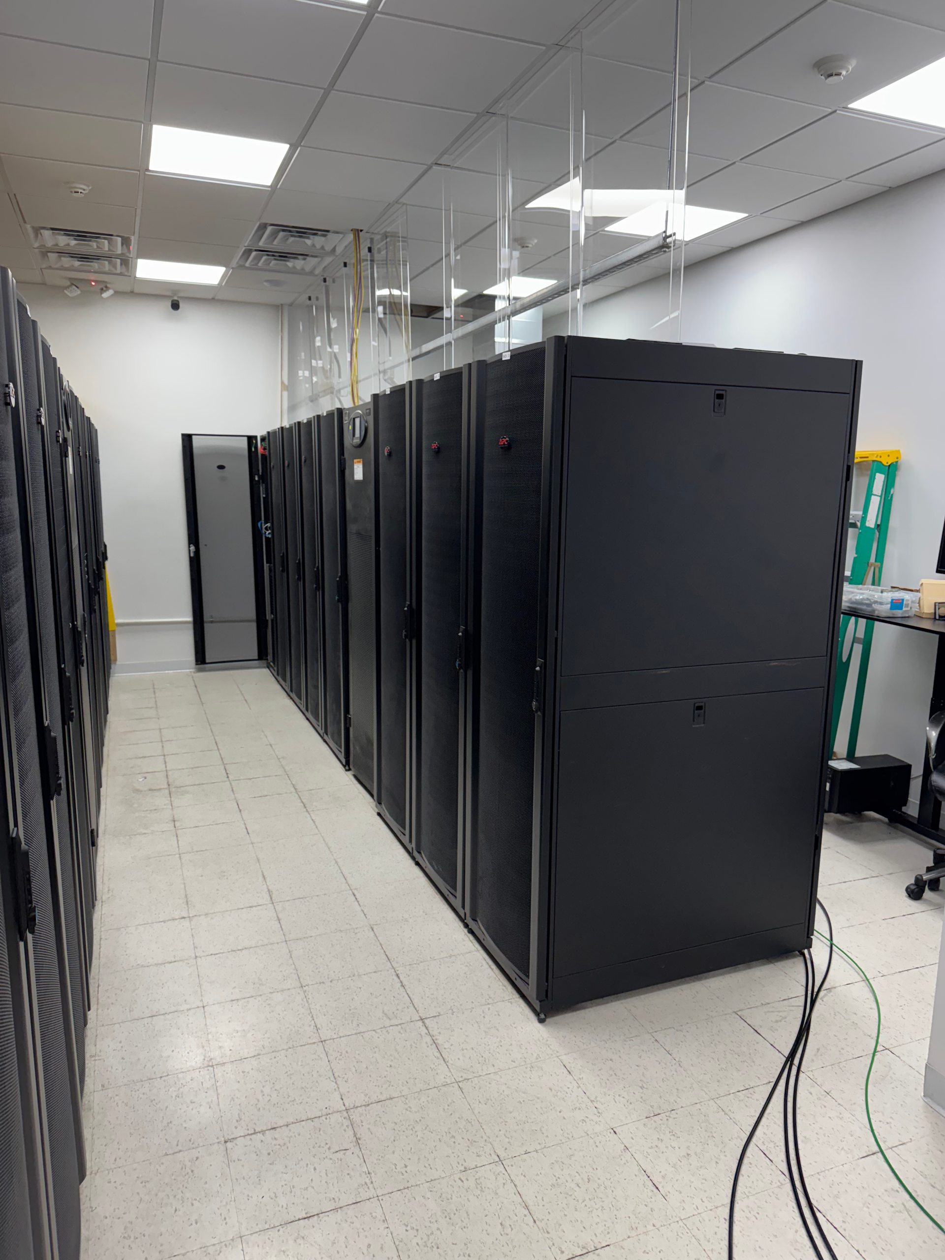Server room with black server racks lining a white-tiled aisle under bright ceiling lights