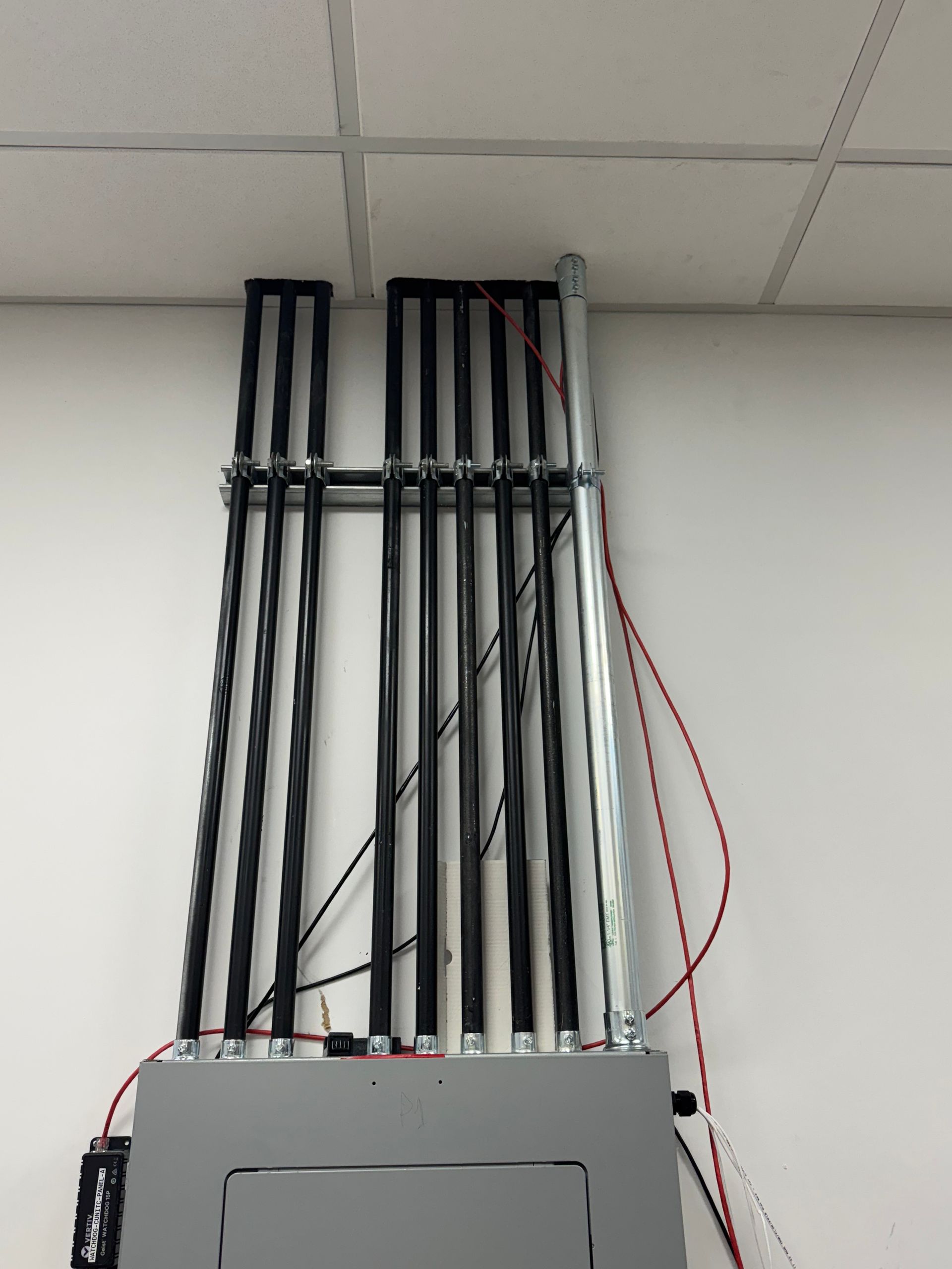 Wall-mounted electrical panel with exposed black and red wiring against a drop ceiling.