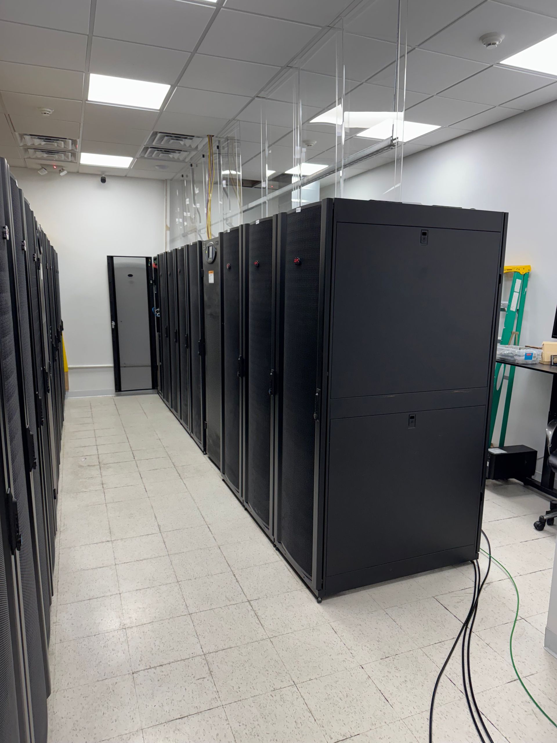 Server room with rows of black equipment racks in a bright tiled room.