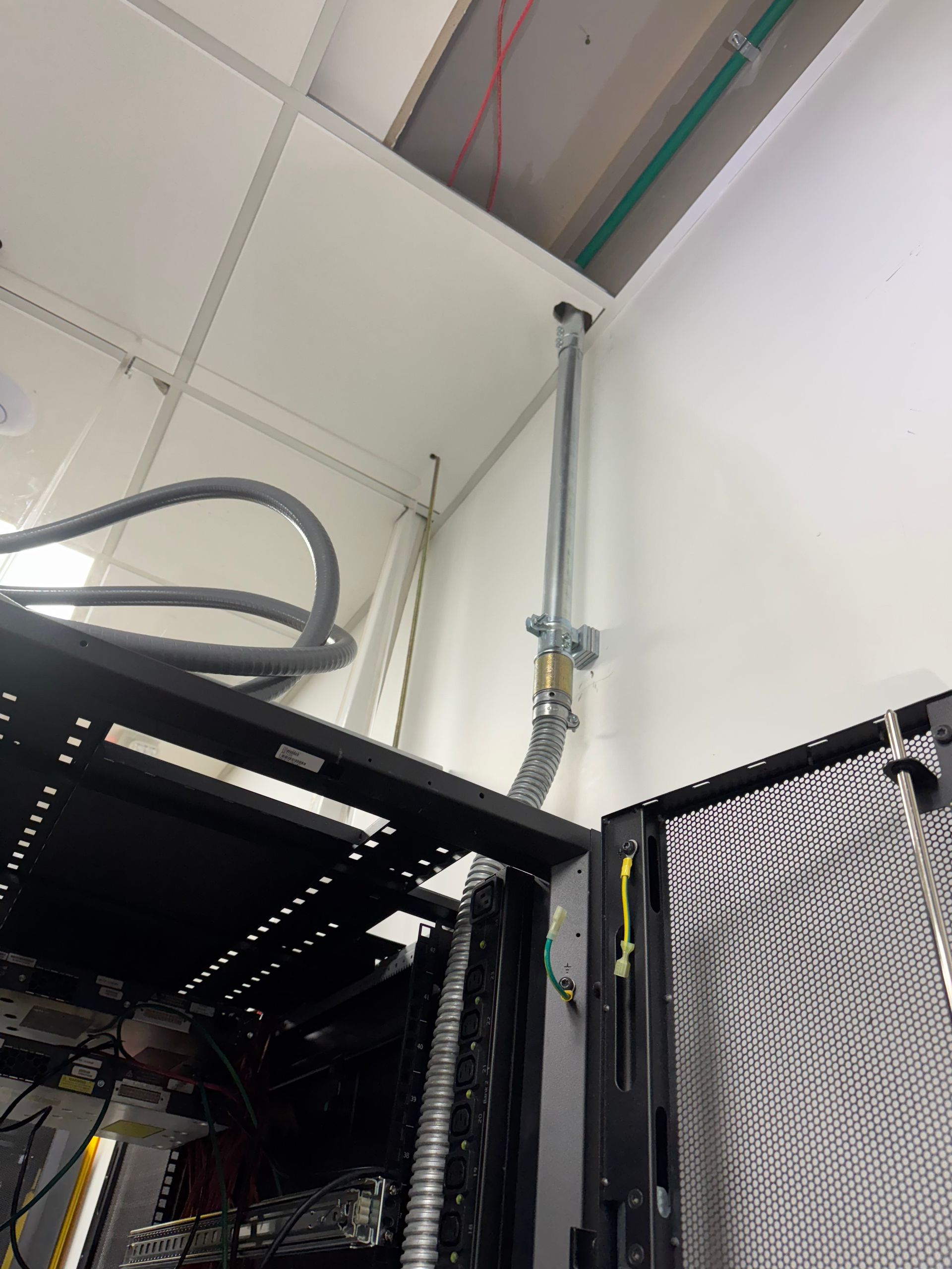 Ceiling corner with exposed conduit and cables above black server racks in a utility room