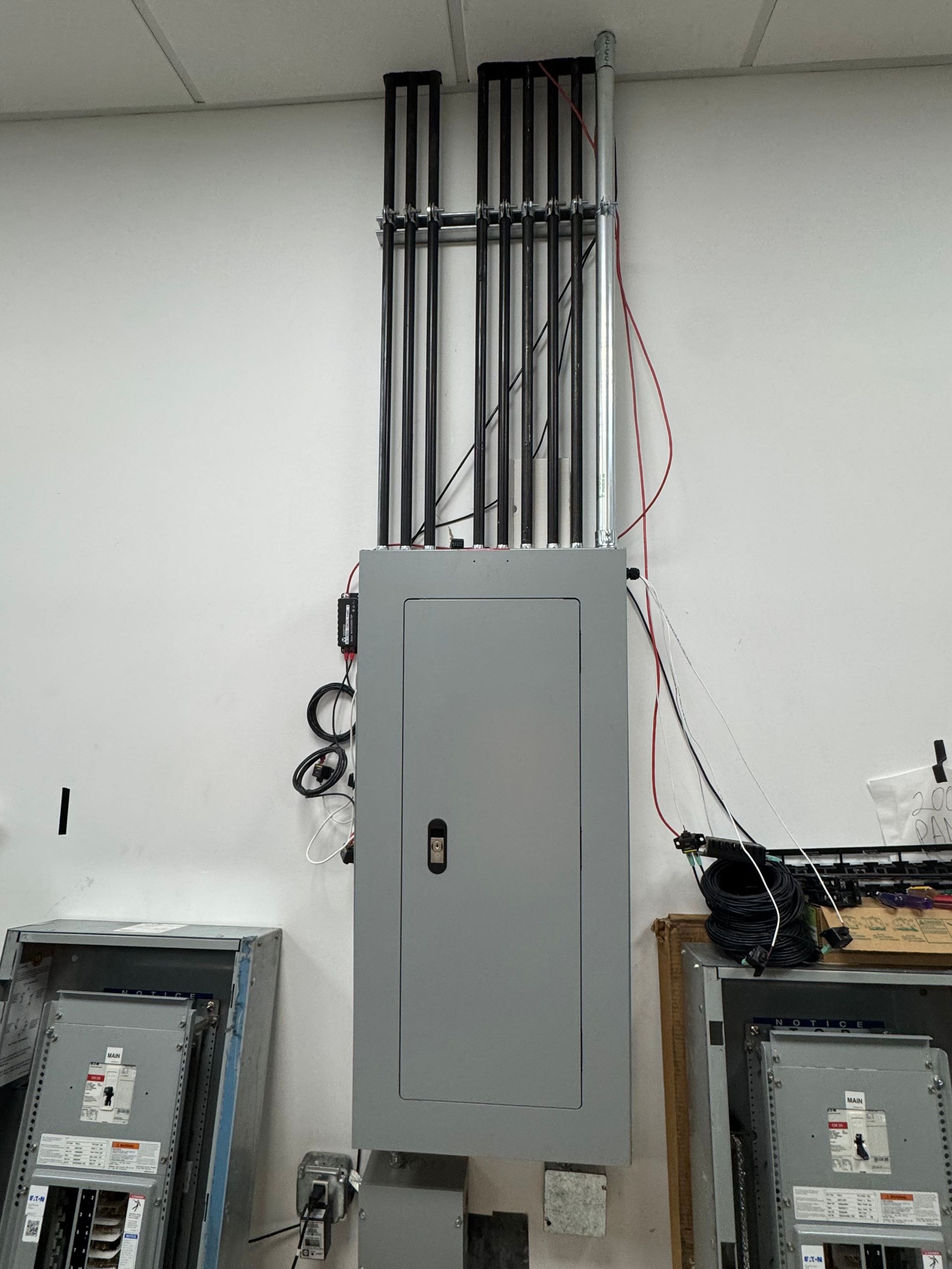 Electrical panel room with a central gray breaker cabinet and exposed conduit, flanked by two smaller panels.