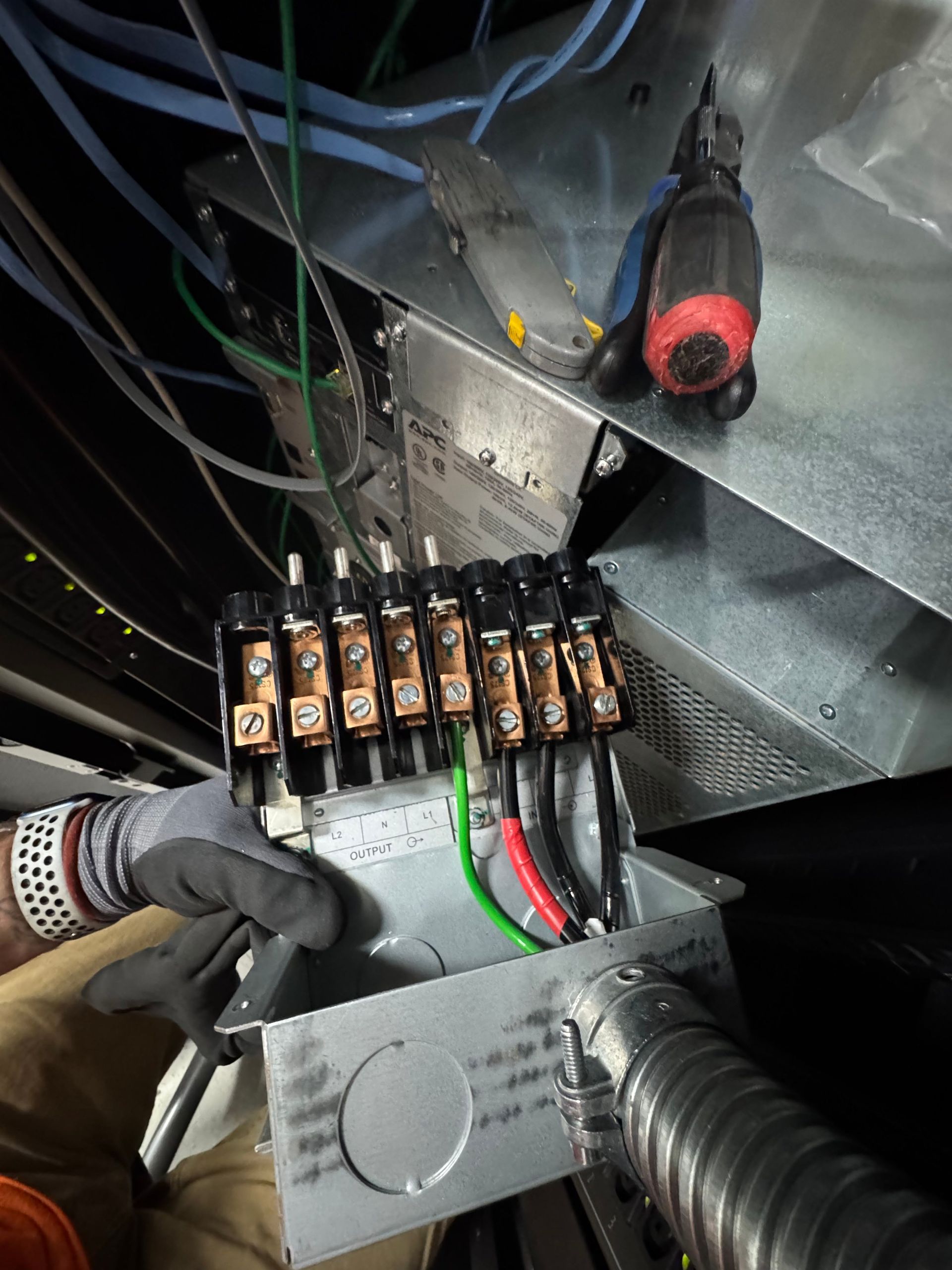 Gloved hand inspecting an electrical control panel with relays, wires, and a flashlight