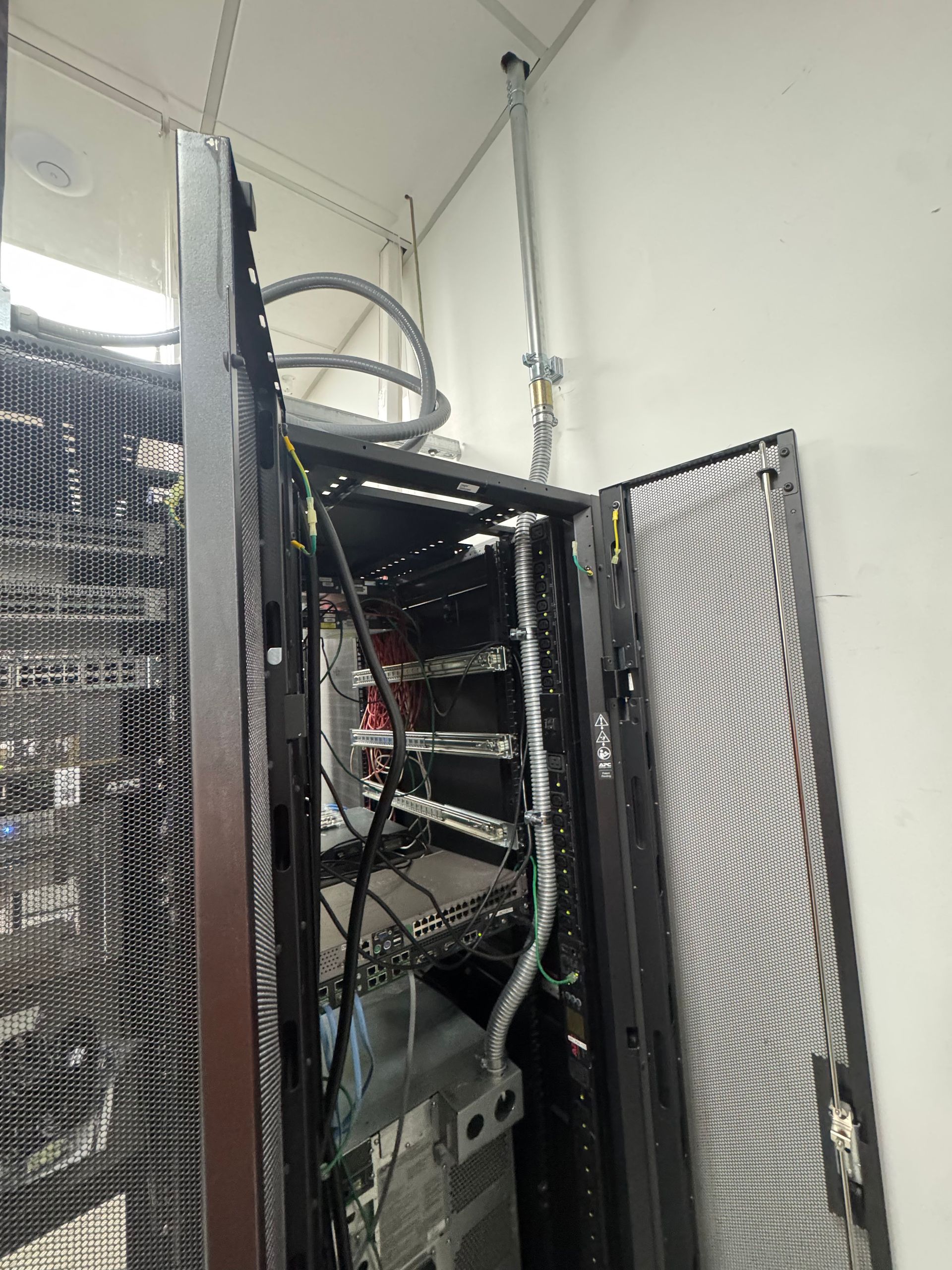 Open server rack with cables and equipment in a white utility room