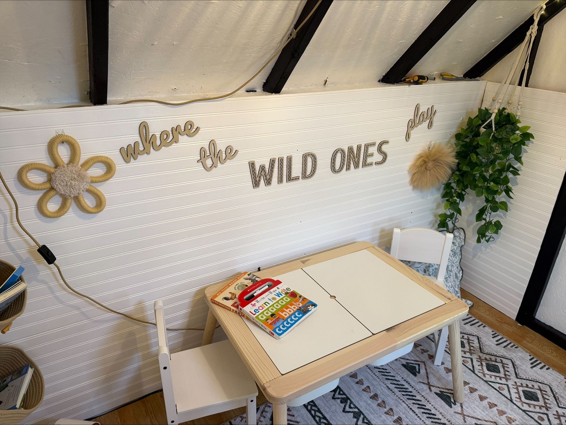 Cozy kids’ art nook with a small table, chairs, wall decor, string lights, and plants in a white room