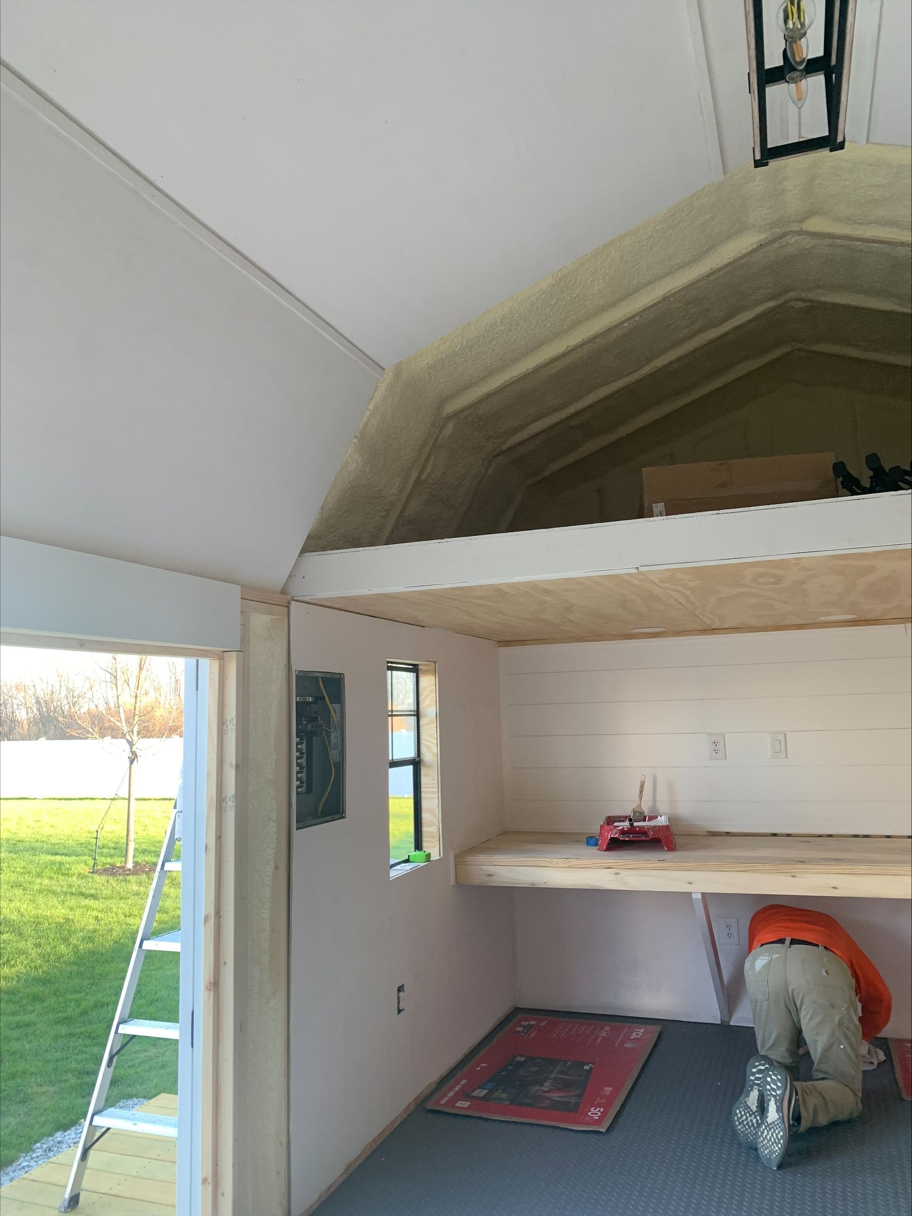 Interior of a small room under construction with an arched ceiling, open doorway, shelves, and a worker crouching.