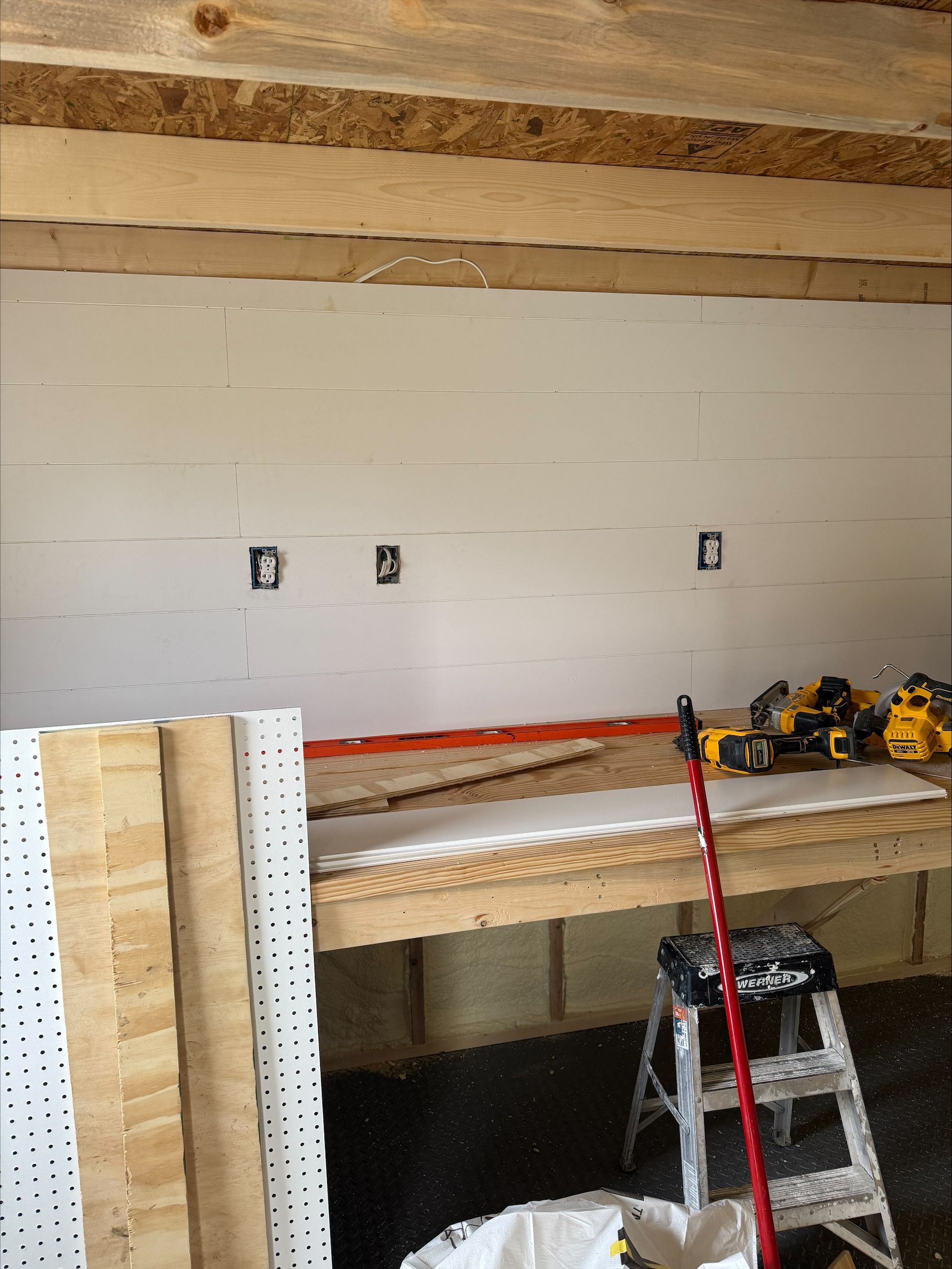 Partially finished room with workbench, ladder, and tools against a white wall.