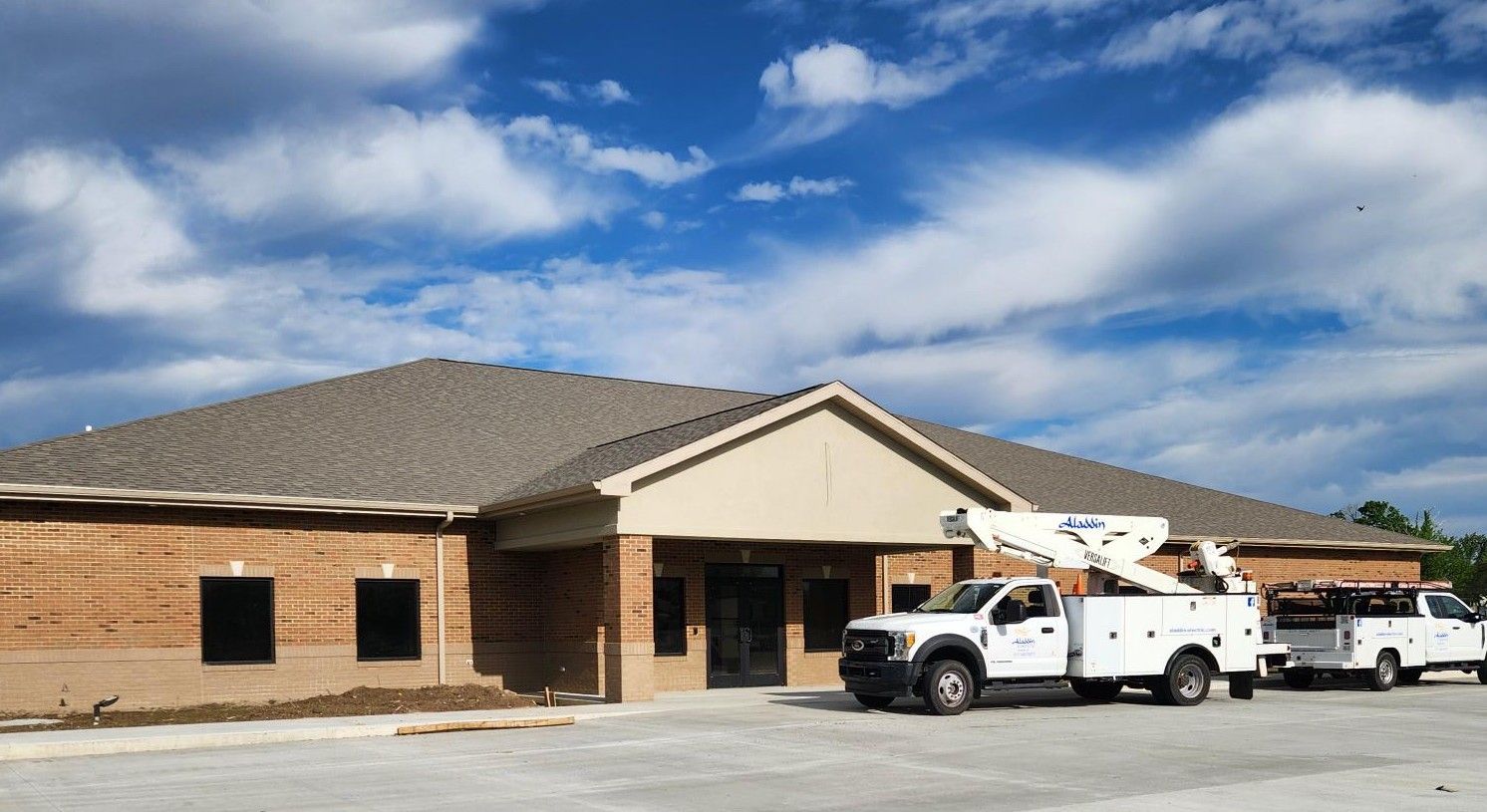 Brick building with tan roof and two white utility trucks parked outside under a blue sky