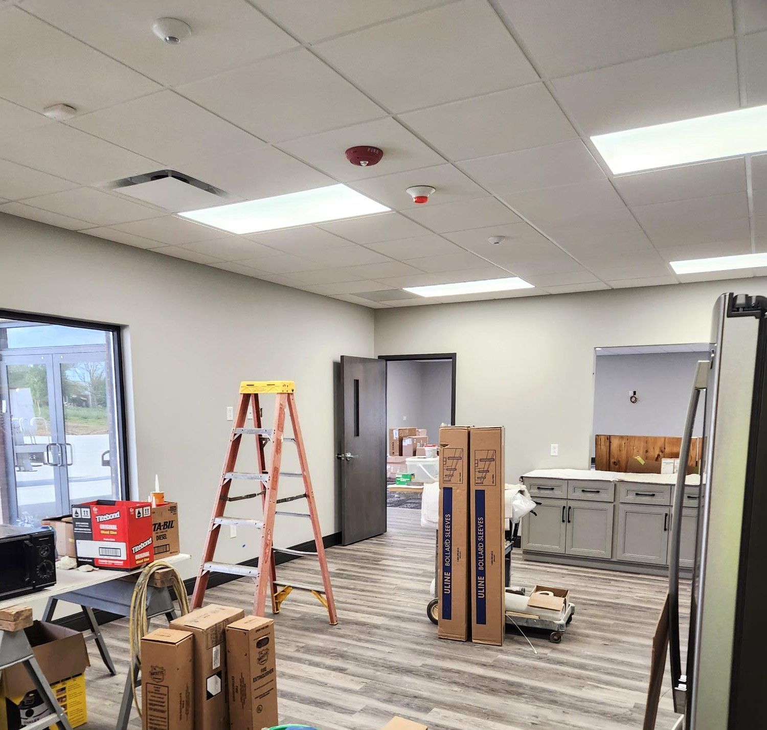 Office under renovation with ladders, boxes, tools, and ceiling lights in a partly finished room