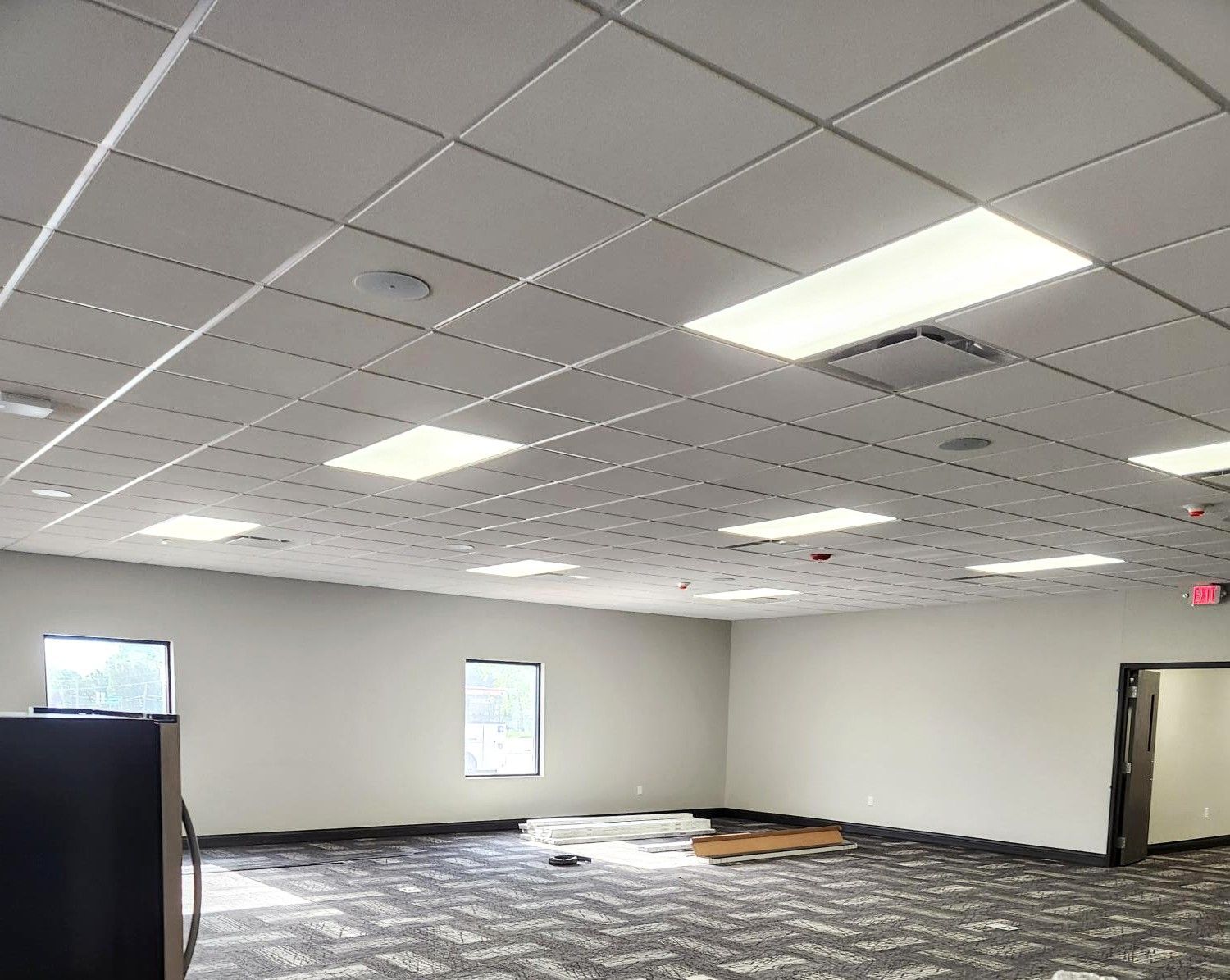Empty office room with patterned carpet, white drop ceiling, and bright recessed lights
