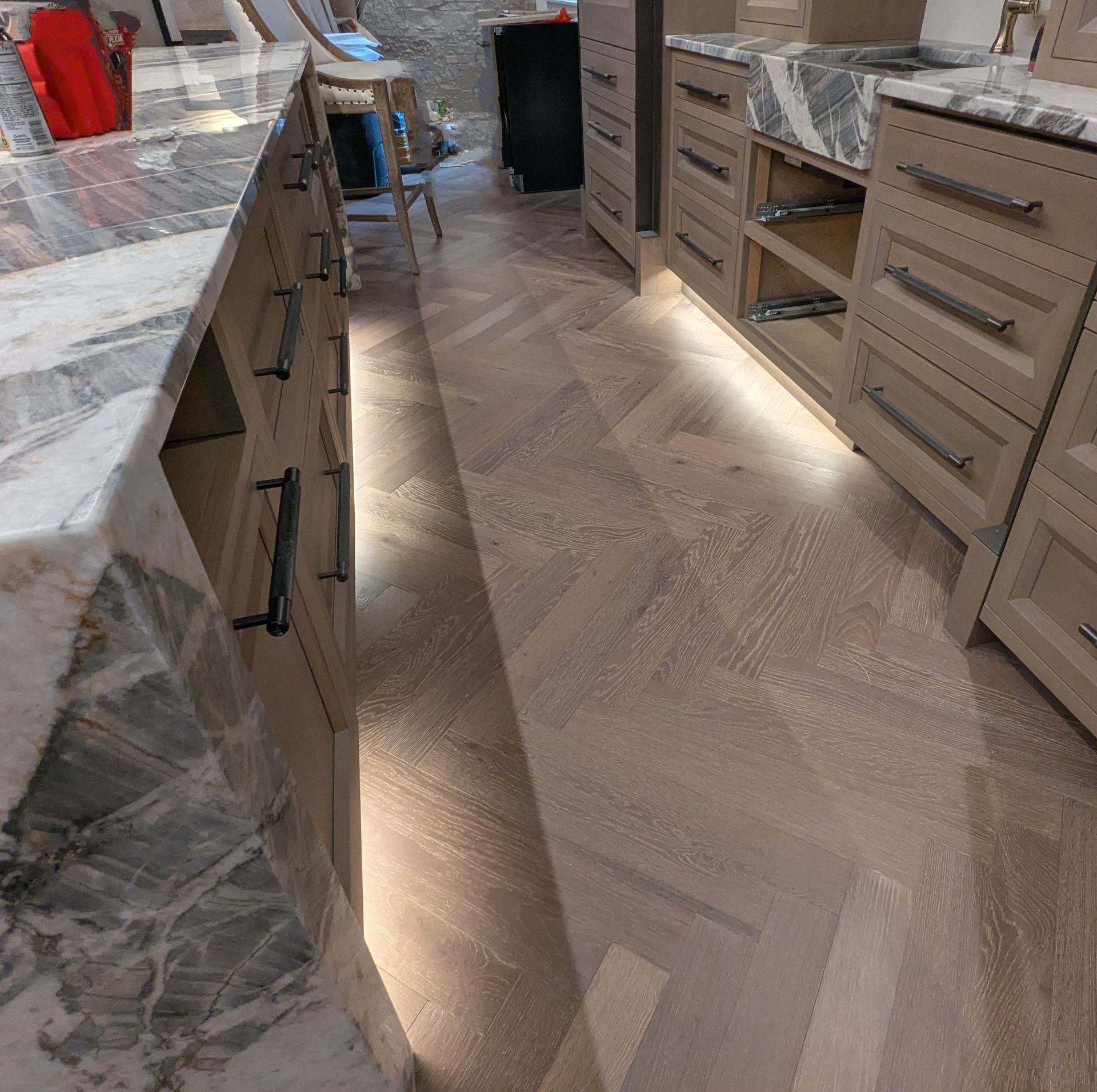 Modern kitchen aisle with beige cabinets, marble countertops, and a light wood herringbone floor