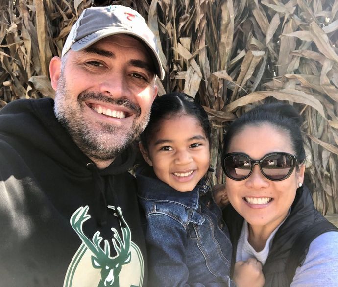 A man , woman and child are posing for a picture in front of a corn field.