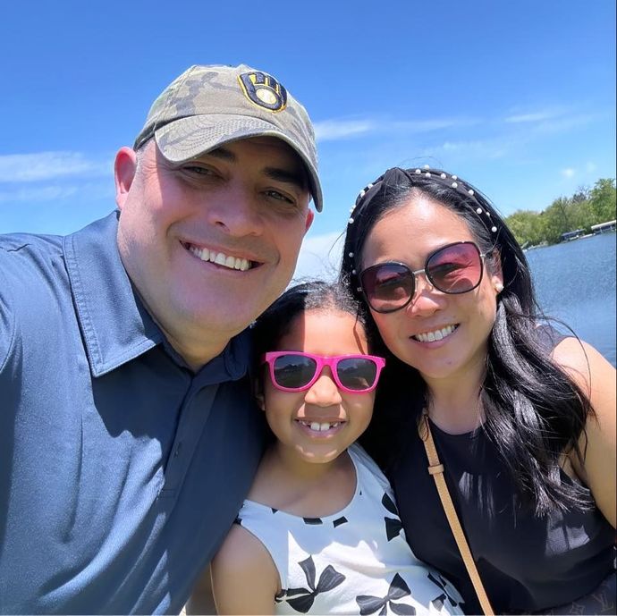 A man and woman are posing for a picture with a little girl wearing pink sunglasses.