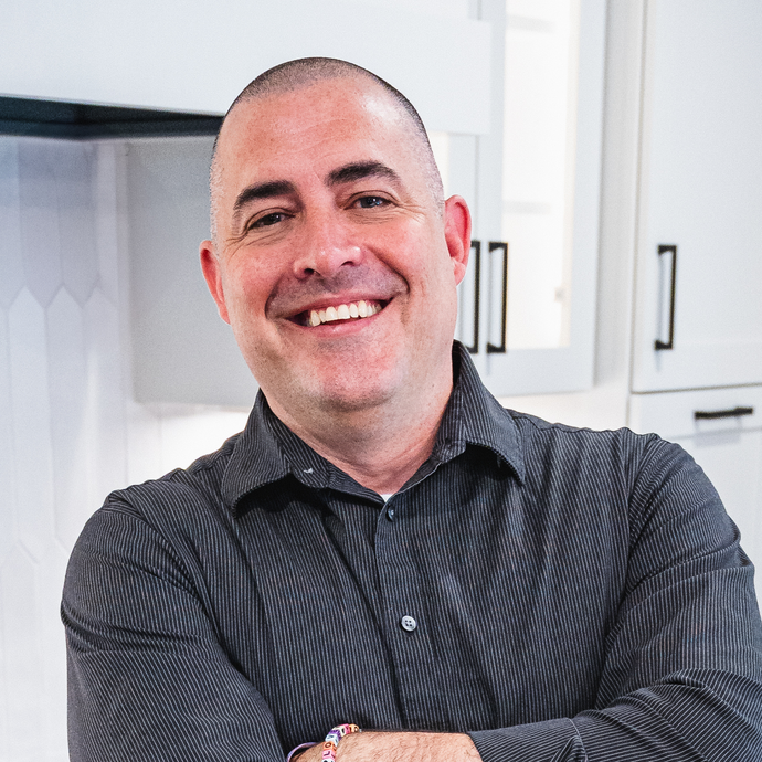 Koby Luedtke A man in a striped shirt is smiling with his arms crossed in a kitchen.