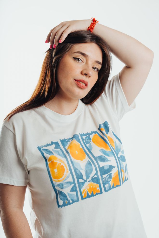 Mujer posando con una camiseta blanca estampada sobre un fondo liso.