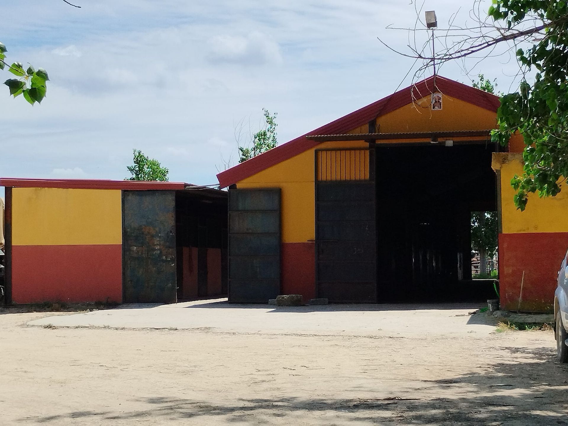 Granero amarillo y rojo con puertas abiertas en un lote de tierra bajo un cielo nublado.